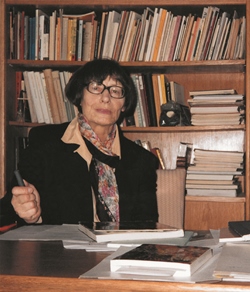 fotografia Anny Różyckiej-Bryzek przy stole, na tle regału z książkami